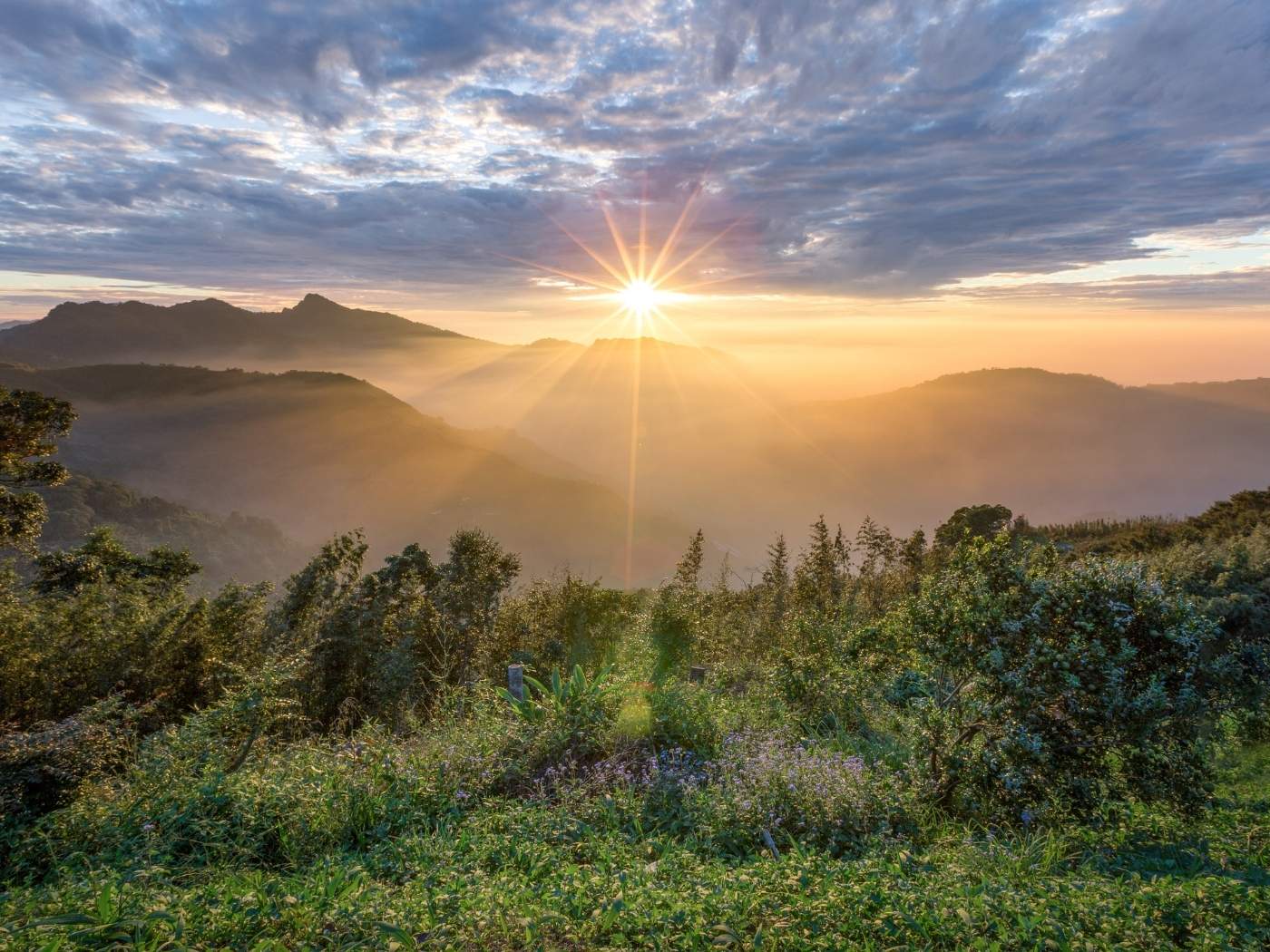Landschaft mit Bergen im Hintergrund, die Sonne geht gerade unter.