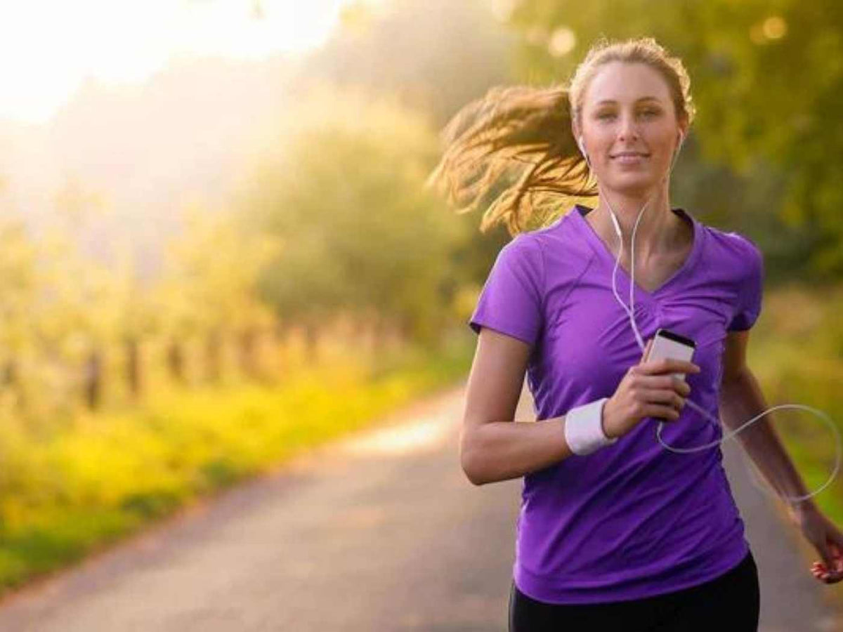 Eine Frau die in der Natur jogged. Sie trägt ein lila T-Shirt und hört Musik