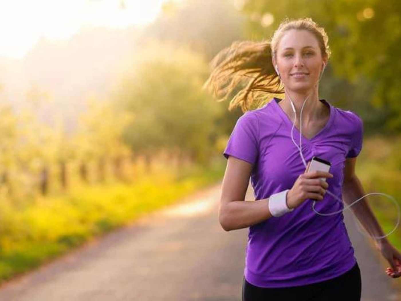 Eine Frau die in der Natur jogged. Sie trägt ein lila T-Shirt und hört Musik
